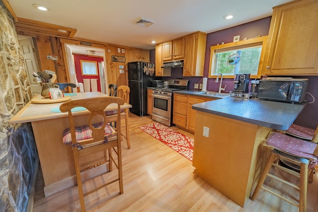 kitchen with dark countertops, light wood-style floors, under cabinet range hood, a sink, and black appliances