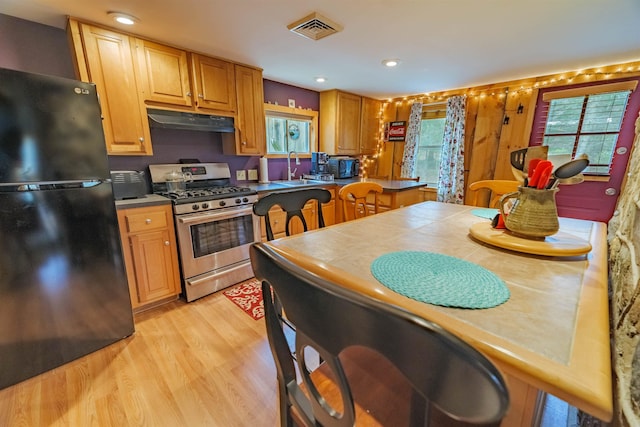 kitchen featuring visible vents, freestanding refrigerator, stainless steel gas range oven, under cabinet range hood, and light wood finished floors