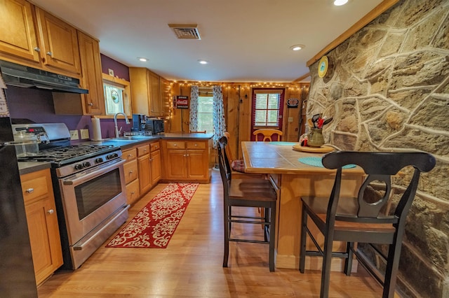 kitchen with visible vents, stainless steel range with gas stovetop, a sink, a peninsula, and light wood-style flooring