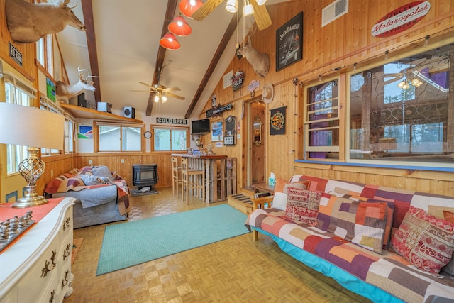 living area featuring a wood stove, high vaulted ceiling, wood walls, a ceiling fan, and beamed ceiling