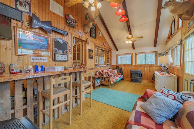 bedroom with visible vents, a wood stove, beam ceiling, wooden walls, and high vaulted ceiling
