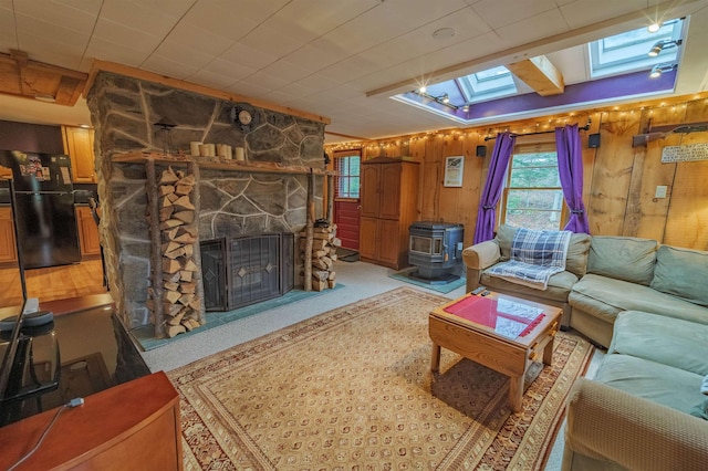 living area featuring a skylight, a fireplace, a wood stove, wood walls, and light carpet