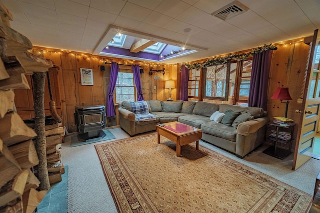 carpeted living room featuring visible vents, a wood stove, wooden walls, and a skylight