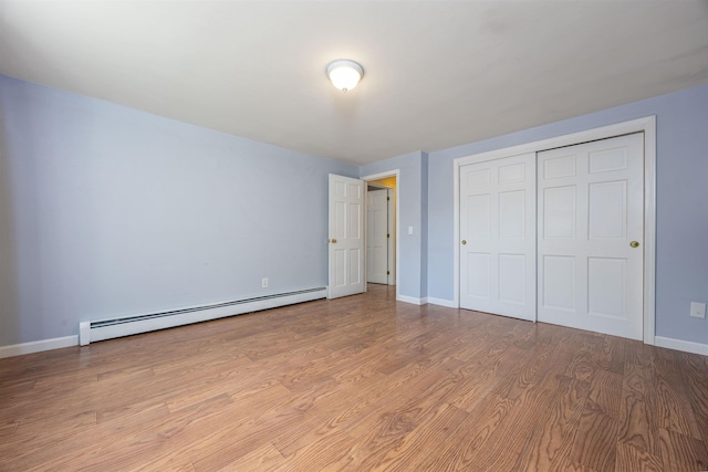 unfurnished bedroom with a closet, baseboards, light wood-type flooring, and a baseboard radiator