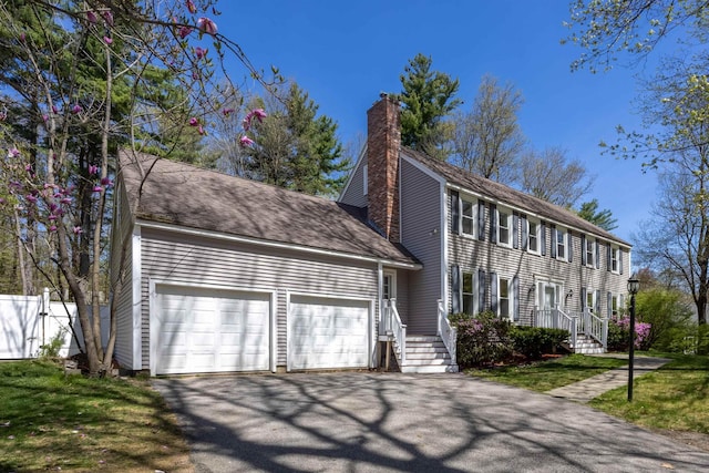 colonial house featuring fence, an attached garage, driveway, and a chimney