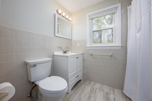 bathroom with vanity, toilet, a wainscoted wall, tile walls, and curtained shower