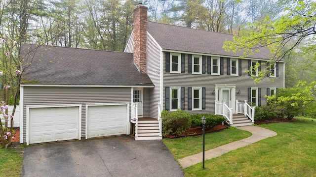 colonial inspired home featuring aphalt driveway, a chimney, roof with shingles, a front lawn, and an attached garage