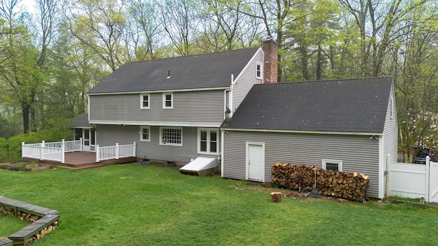 back of house featuring a chimney, roof with shingles, a lawn, and a deck