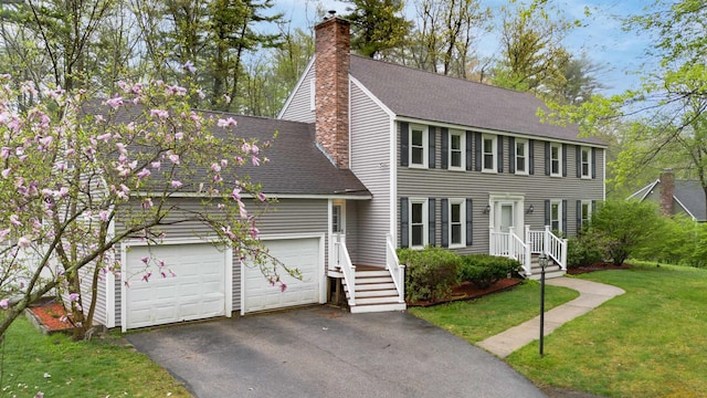 colonial-style house featuring a front yard, a chimney, roof with shingles, and aphalt driveway