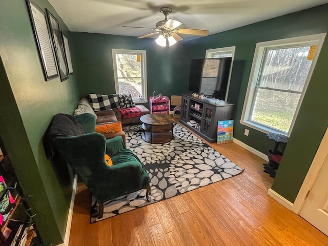 living area featuring a ceiling fan, baseboards, and wood finished floors