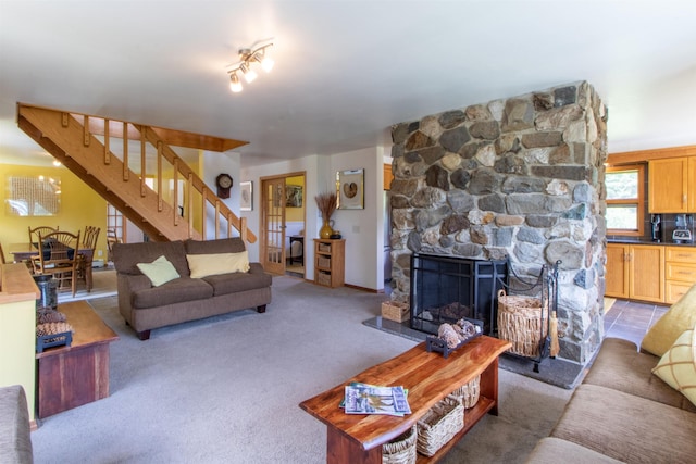 carpeted living room with a stone fireplace and stairway