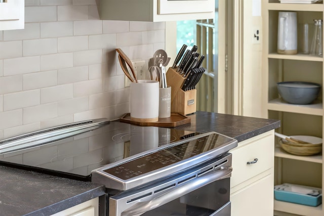 interior details featuring backsplash, dark countertops, stainless steel electric stove, and white cabinets