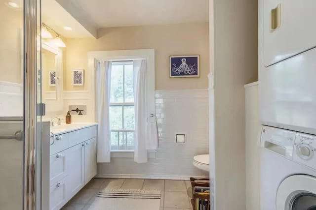 bathroom with tile walls, wainscoting, tile patterned floors, vanity, and stacked washer and clothes dryer