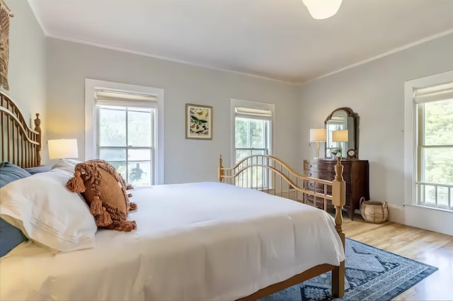 bedroom with ornamental molding, multiple windows, and wood finished floors