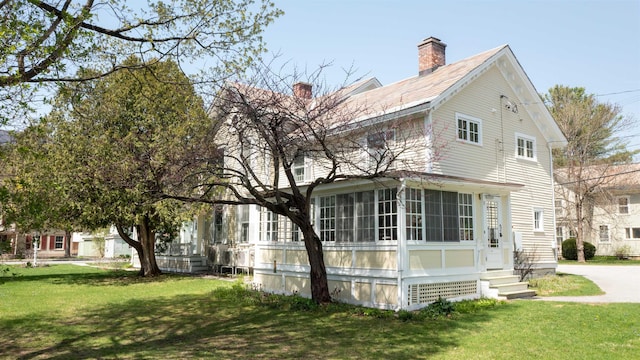 exterior space featuring entry steps, a yard, a chimney, and a sunroom