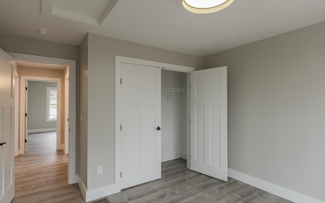 unfurnished bedroom with a closet, baseboards, attic access, and wood finished floors