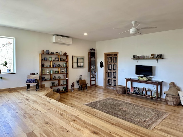 living area featuring ceiling fan, a wall unit AC, and hardwood / wood-style flooring