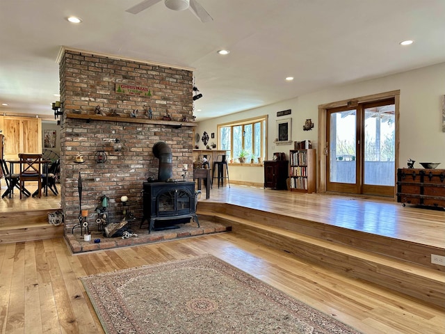 living area with ceiling fan, wood-type flooring, a wood stove, and recessed lighting