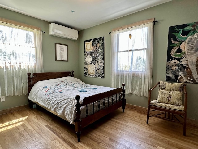 bedroom with light wood finished floors, a wall unit AC, and multiple windows