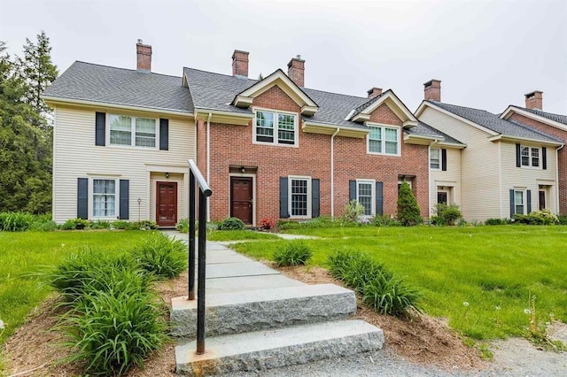 view of property with a chimney, brick siding, and a front yard