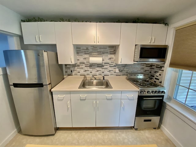 kitchen with white cabinets, appliances with stainless steel finishes, a sink, light countertops, and tasteful backsplash