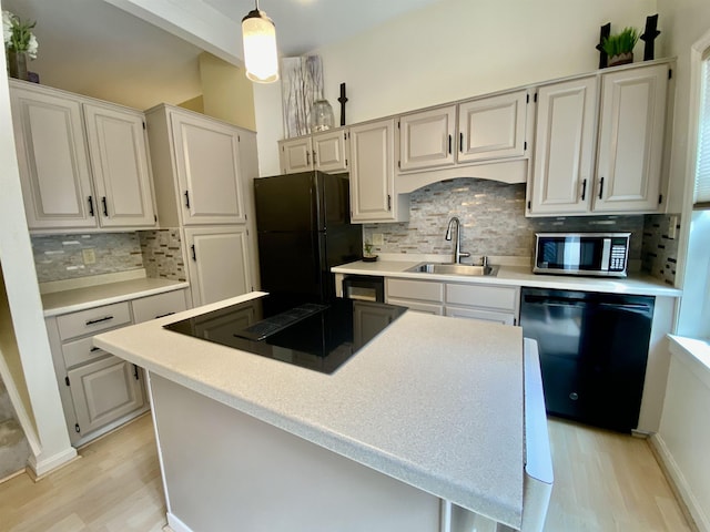kitchen with a sink, decorative backsplash, black appliances, and light wood-style flooring