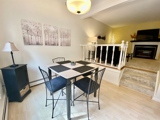 dining area featuring wood finished floors, a baseboard radiator, a glass covered fireplace, and beam ceiling