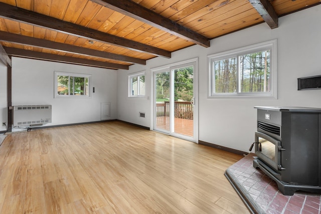 unfurnished living room with a wood stove, beam ceiling, baseboards, heating unit, and light wood-style flooring
