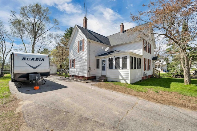 view of side of property with roof with shingles, entry steps, a chimney, a lawn, and driveway