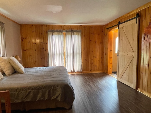 bedroom featuring a barn door, wood finished floors, baseboards, wooden walls, and ornamental molding