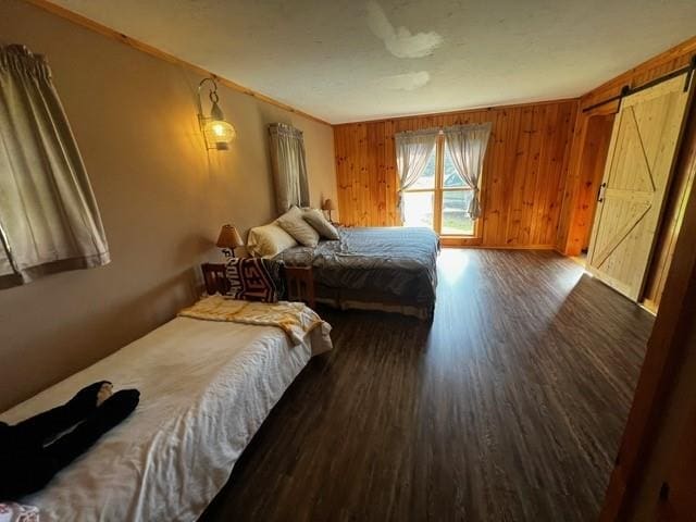 bedroom featuring crown molding, wood walls, a barn door, wood finished floors, and baseboards