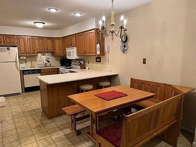 kitchen with light countertops, a peninsula, a chandelier, light floors, and white appliances