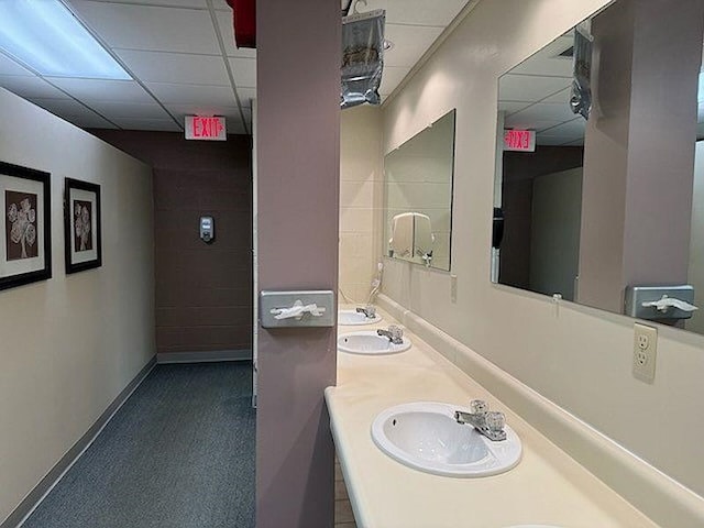 bathroom with double vanity, baseboards, a drop ceiling, and a sink