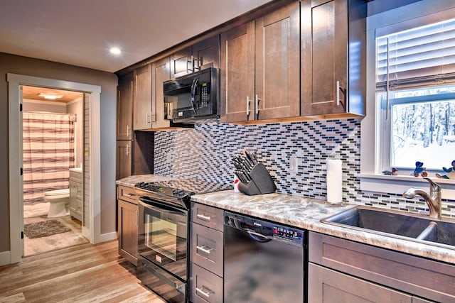 kitchen featuring a sink, light wood-style flooring, baseboards, backsplash, and black appliances