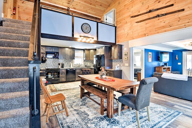 dining space featuring light wood-style floors, high vaulted ceiling, wood walls, wood ceiling, and stairway