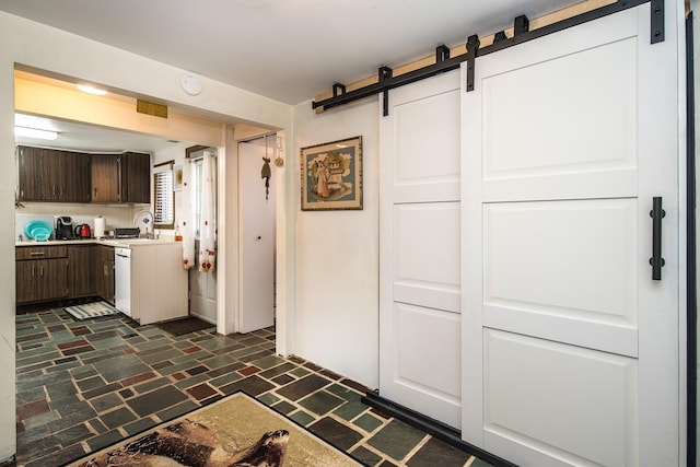 kitchen featuring dark brown cabinetry, white dishwasher, a barn door, light countertops, and a sink