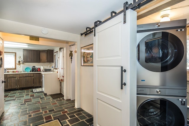 washroom featuring laundry area, stacked washer and clothes dryer, stone finish floor, a barn door, and a sink