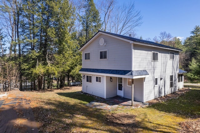 exterior space with roof with shingles and a lawn