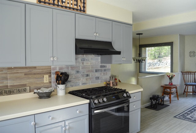 kitchen featuring light countertops, range with gas stovetop, decorative backsplash, light wood-type flooring, and under cabinet range hood