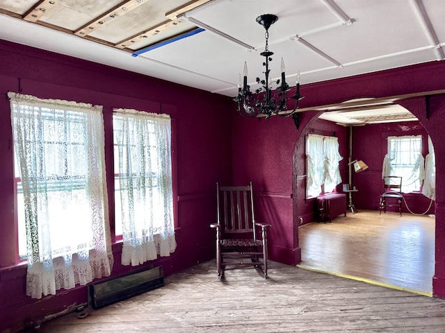 living area with a chandelier, wood finished floors, arched walkways, and radiator heating unit