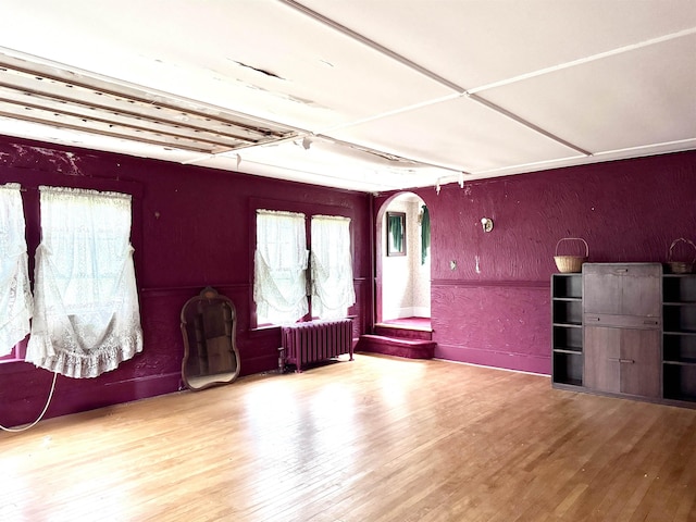 living area featuring wood finished floors, arched walkways, and radiator heating unit