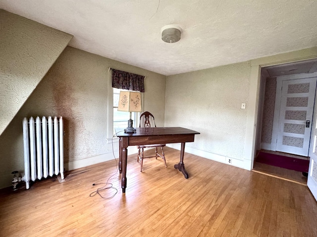 office space with radiator heating unit, a textured ceiling, light wood-style flooring, a textured wall, and baseboards