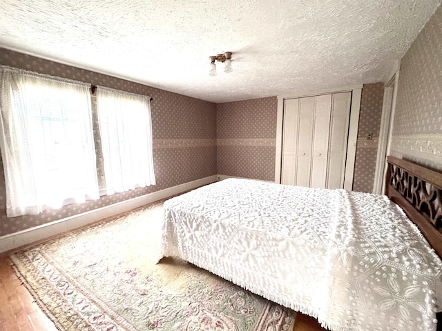 bedroom with wallpapered walls, a textured ceiling, a closet, and baseboards