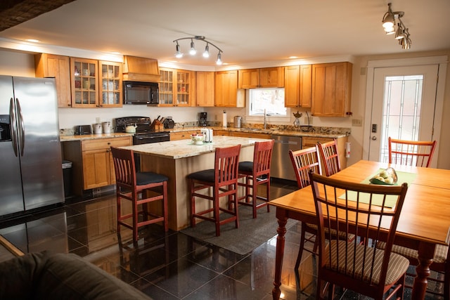 kitchen with a kitchen breakfast bar, a kitchen island, track lighting, black appliances, and glass insert cabinets