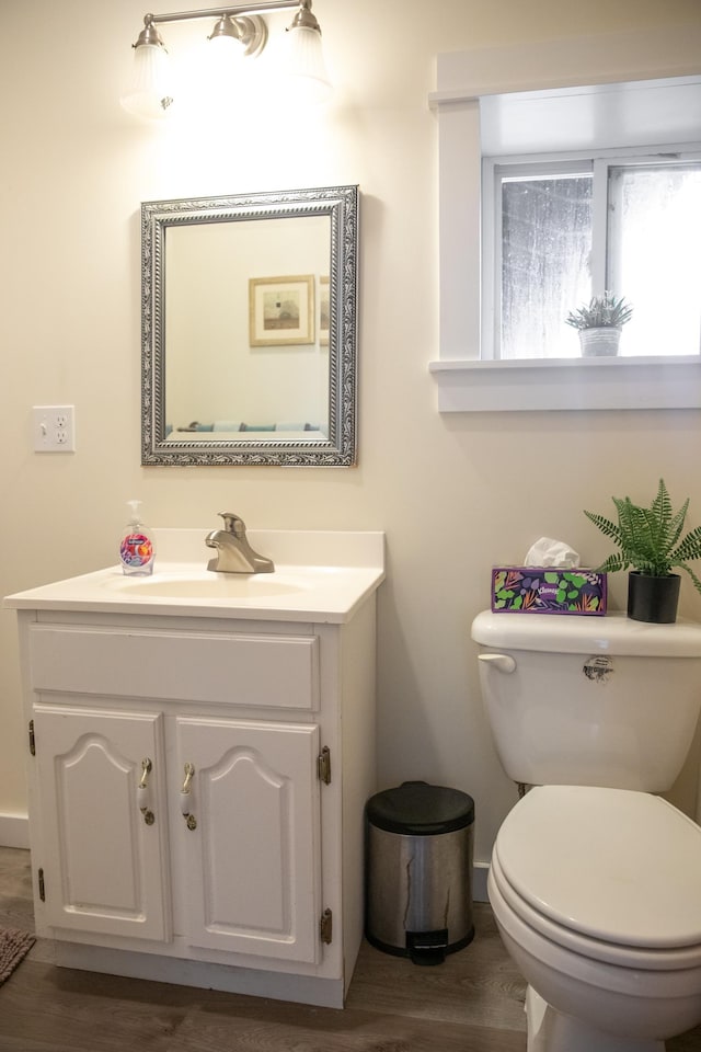 half bathroom featuring vanity, baseboards, wood finished floors, and toilet