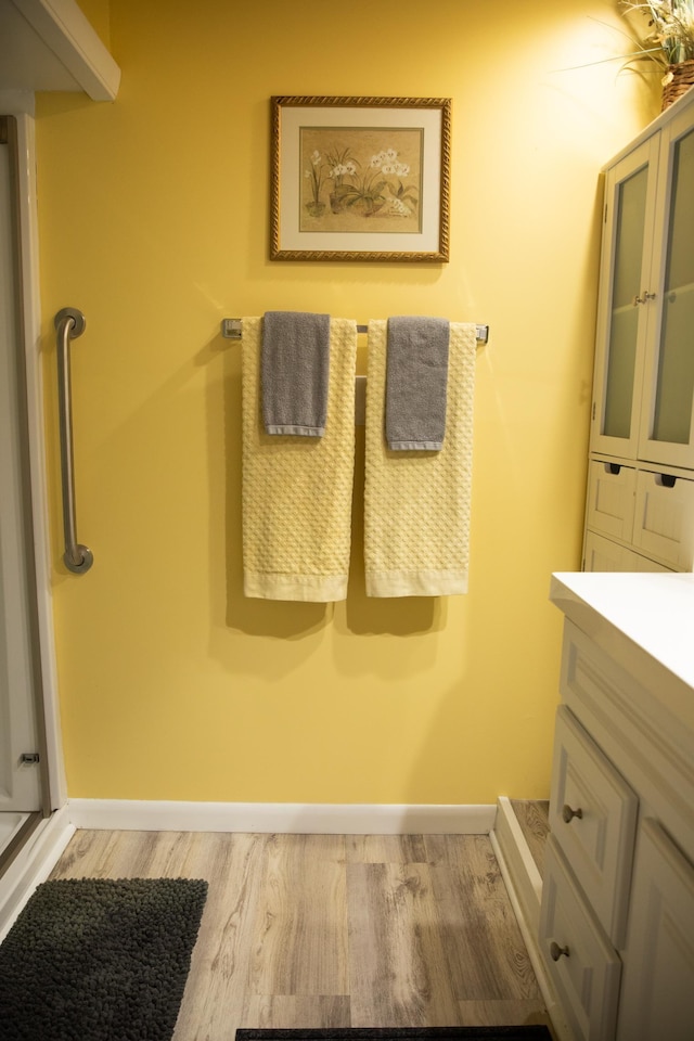 full bath with baseboards, a shower with door, vanity, and wood finished floors