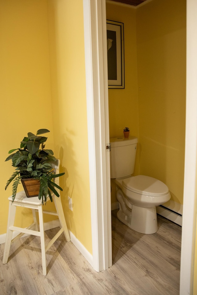 bathroom with toilet, baseboards, a baseboard heating unit, and wood finished floors