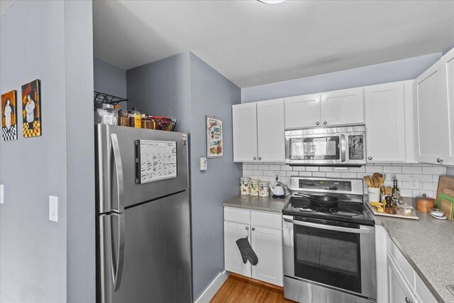 kitchen featuring appliances with stainless steel finishes, tasteful backsplash, white cabinetry, and wood finished floors