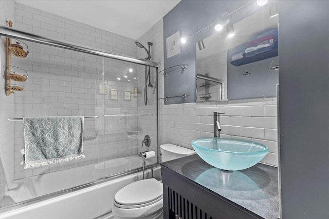 full bath featuring vanity, toilet, shower / bath combination with glass door, and tile walls