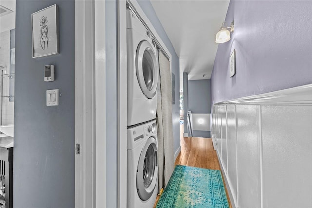 clothes washing area with laundry area, stacked washer and dryer, and wood finished floors